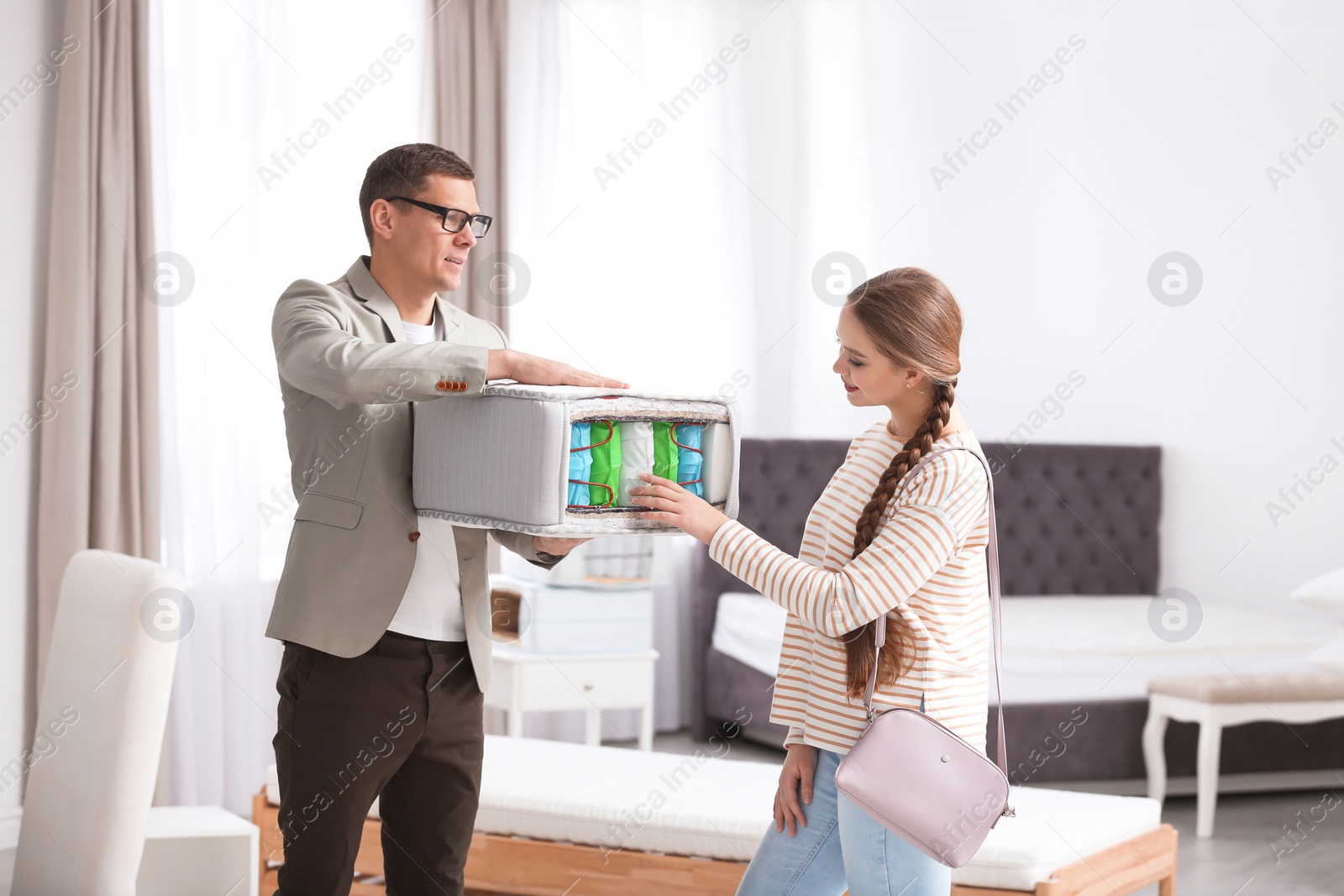 Photo of Salesman showing young woman section of mattress in store