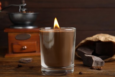 Scented candle with burning wooden wick, coffee beans and chocolate on table