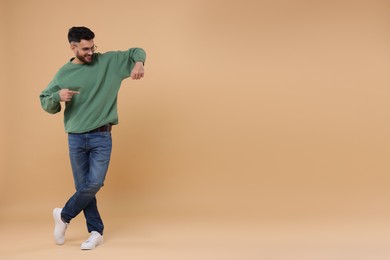 Happy young man pointing at something on beige background, space for text