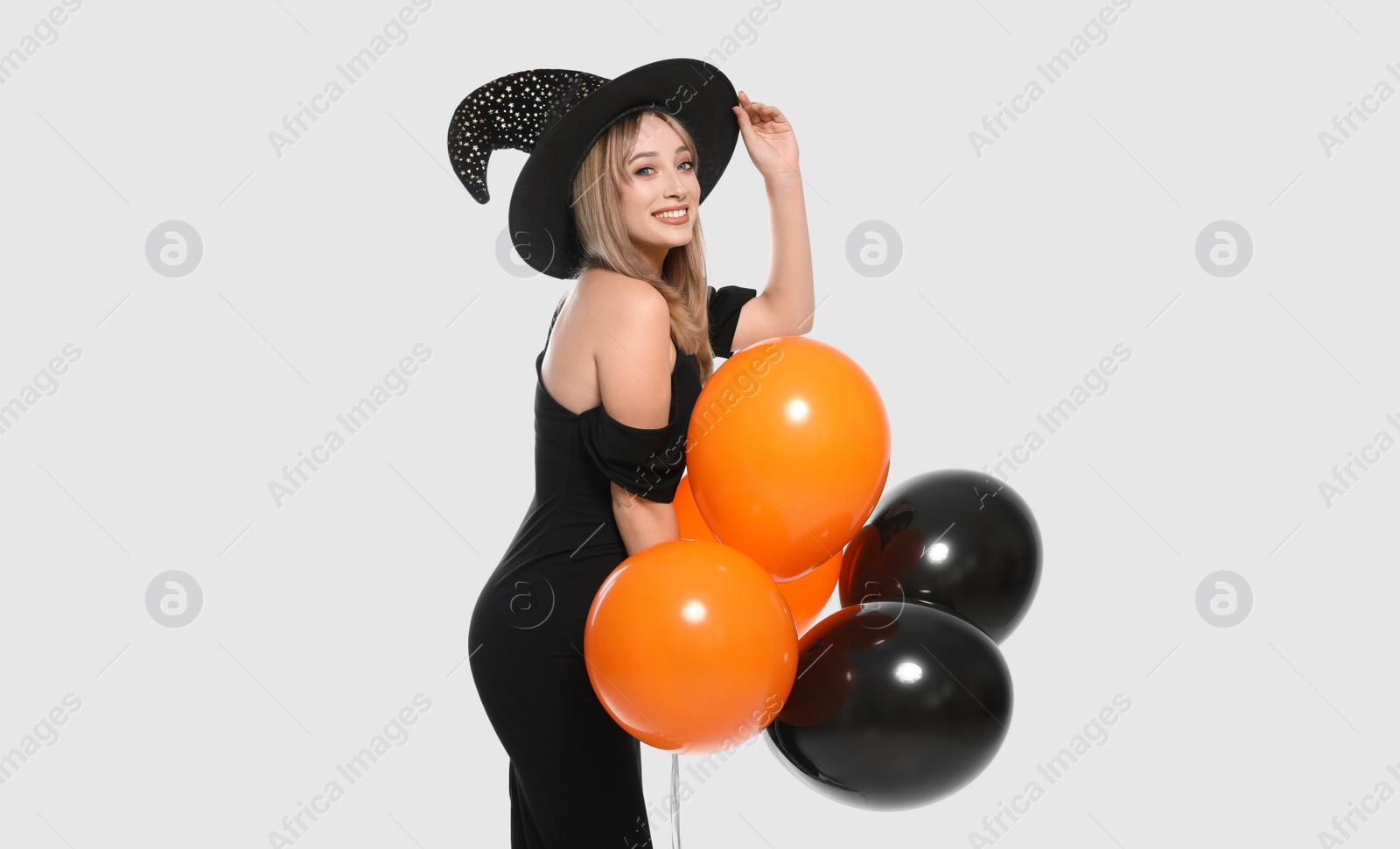 Photo of Beautiful woman in witch costume with balloons on white background. Halloween party