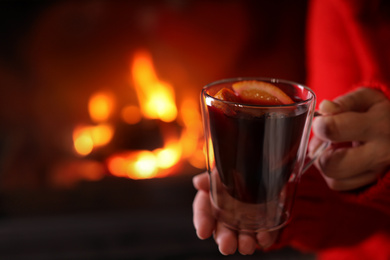 Photo of Woman with tasty mulled wine near burning fireplace indoors, closeup