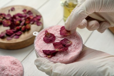 Photo of Woman putting flower petals in bath bomb mold at white table, closeup