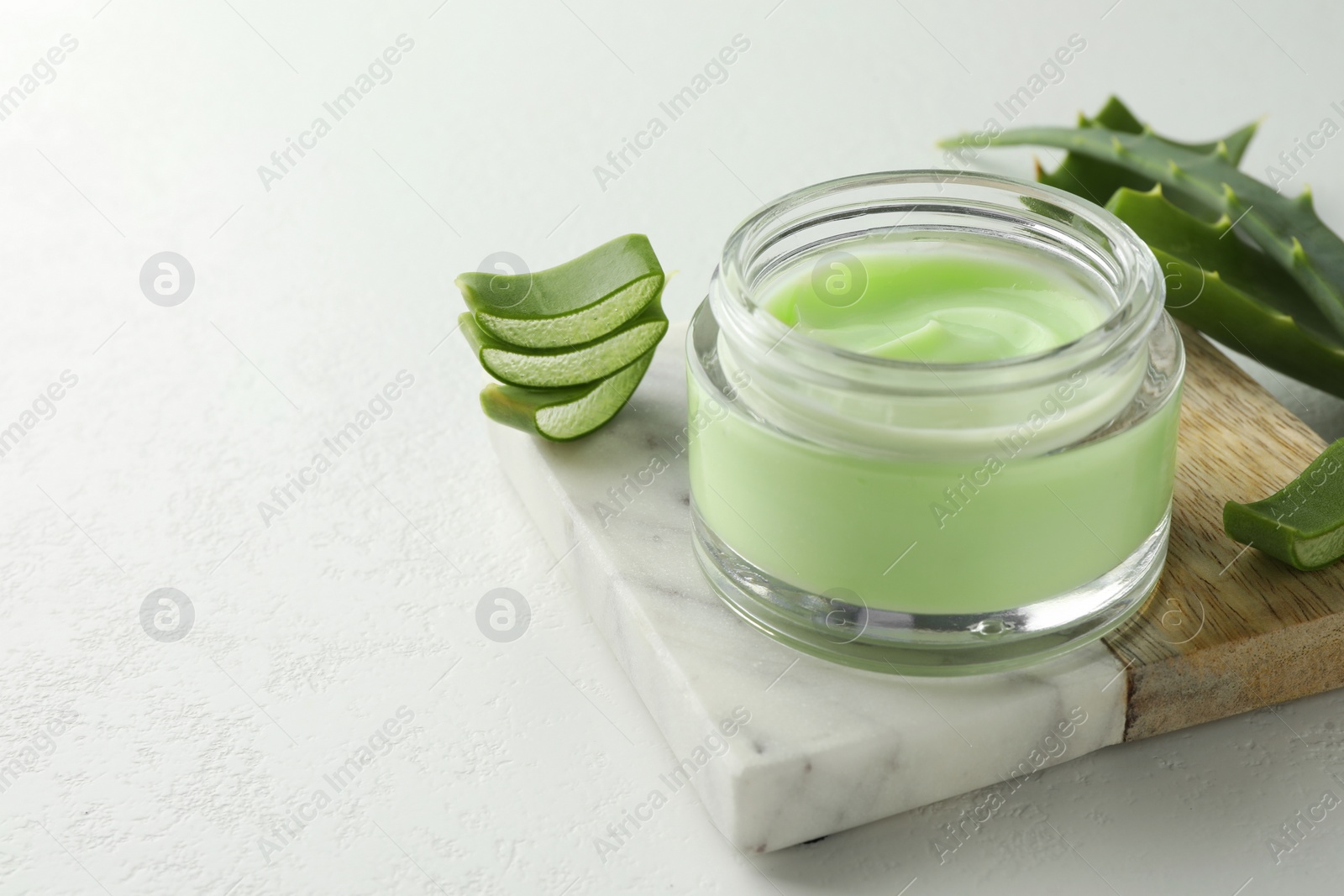 Photo of Jar with cream and cut aloe leaves on white table, closeup. Space for text
