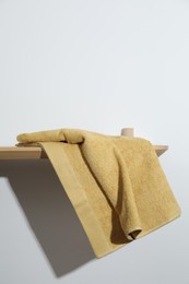 Yellow terry towel on wooden shelf near white wall