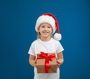 Photo of Cute little child wearing Santa hat with Christmas gift on blue background
