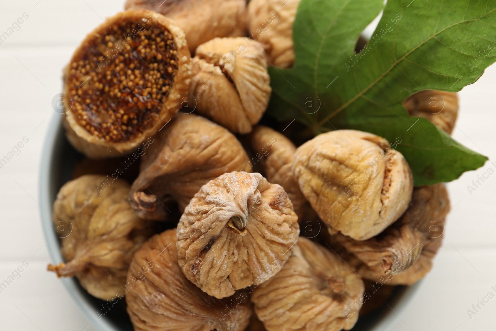 Photo of Bowl with tasty dried figs and green leaf on white table, top view