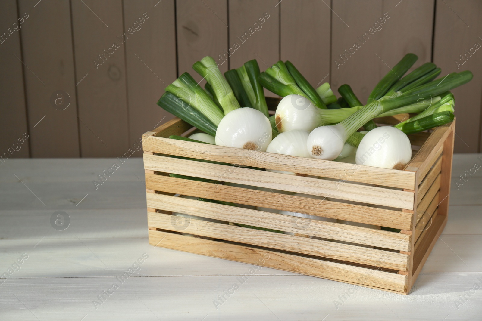 Photo of Crate with green spring onions on white wooden table, space for text