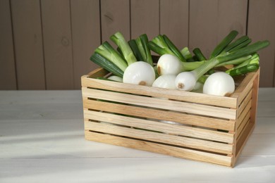 Crate with green spring onions on white wooden table, space for text