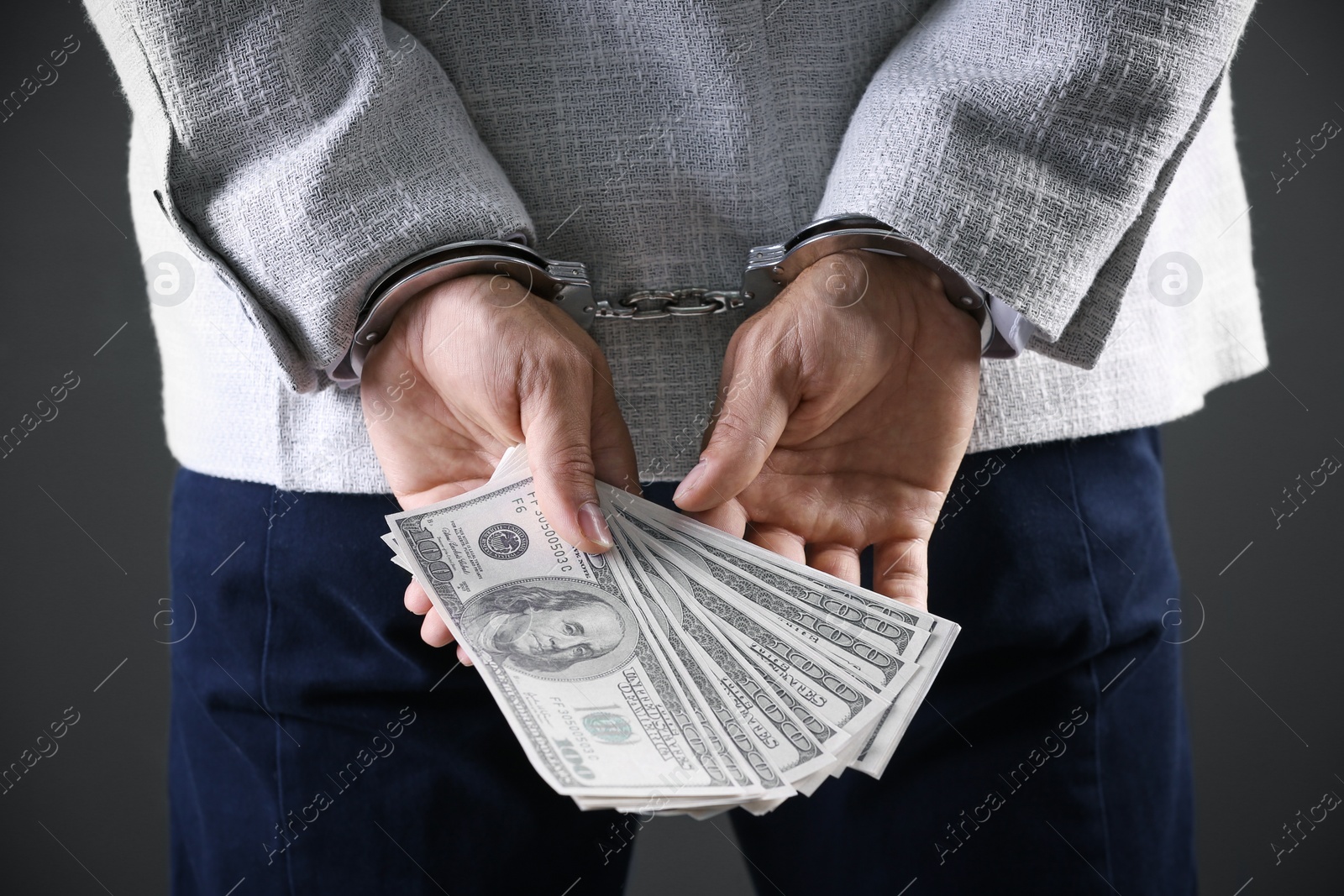 Photo of Man in handcuffs holding bribe money on dark background, closeup