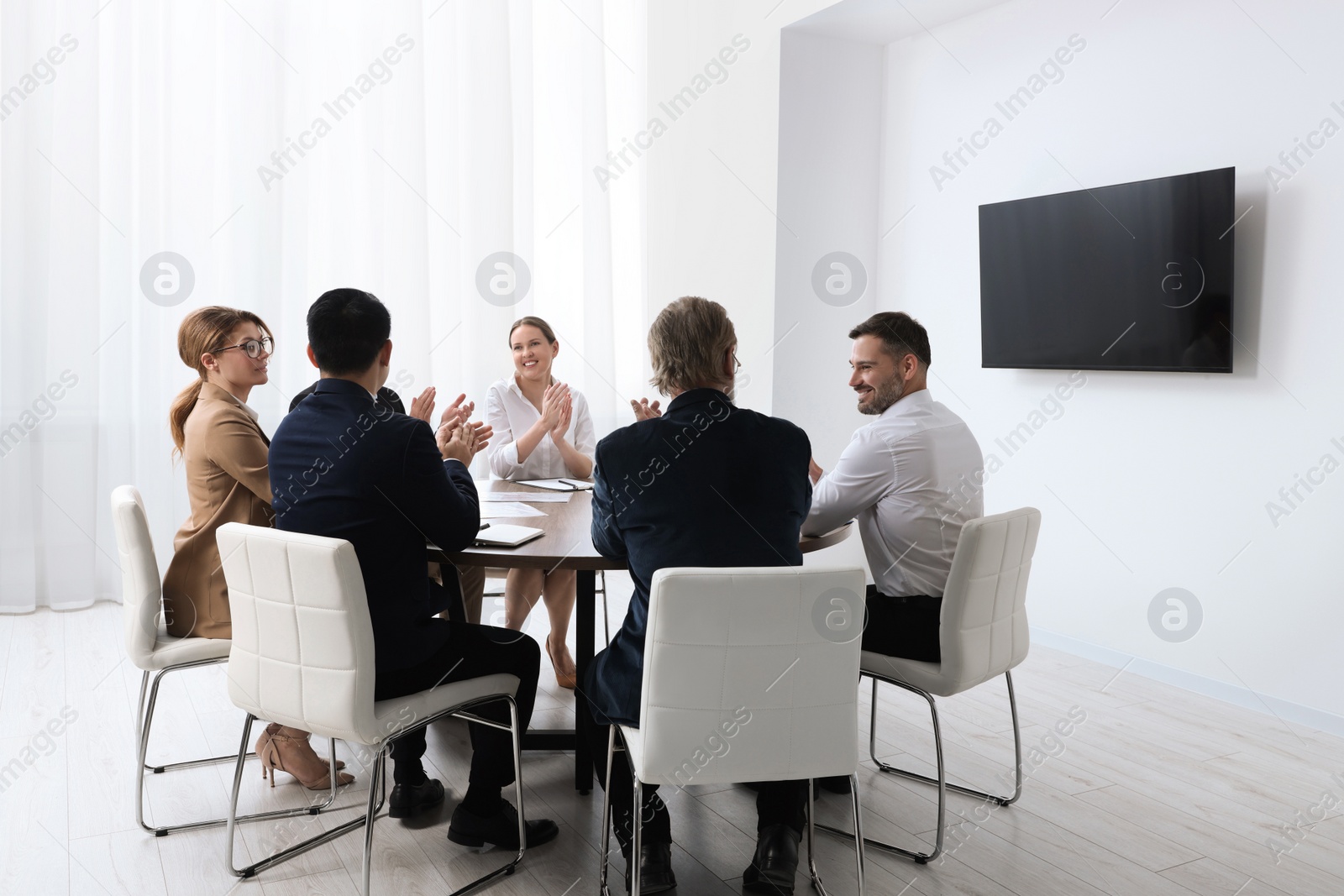 Photo of Business conference. Group of people watching presentation on tv screen in meeting room