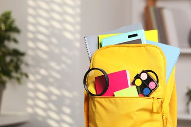 Photo of Yellow backpack with different school stationery indoors, closeup. Space for text