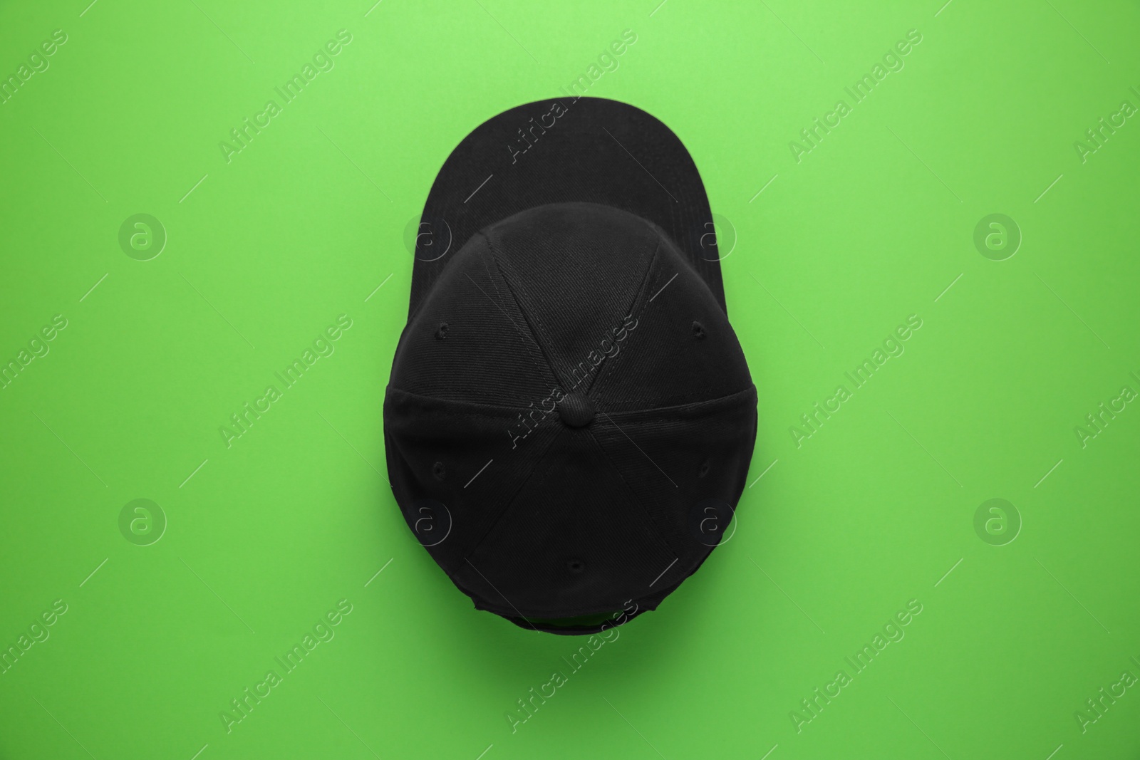 Photo of Stylish black baseball cap on light green background, top view