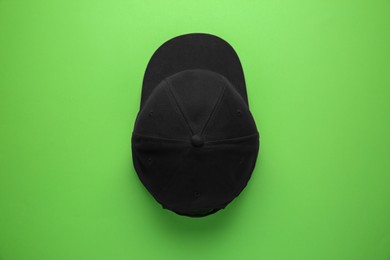 Photo of Stylish black baseball cap on light green background, top view