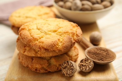 Nutmeg powder, seeds and tasty cookies on wooden board, closeup