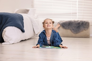 Photo of Cute little girl with book on warm floor at home. Heating system