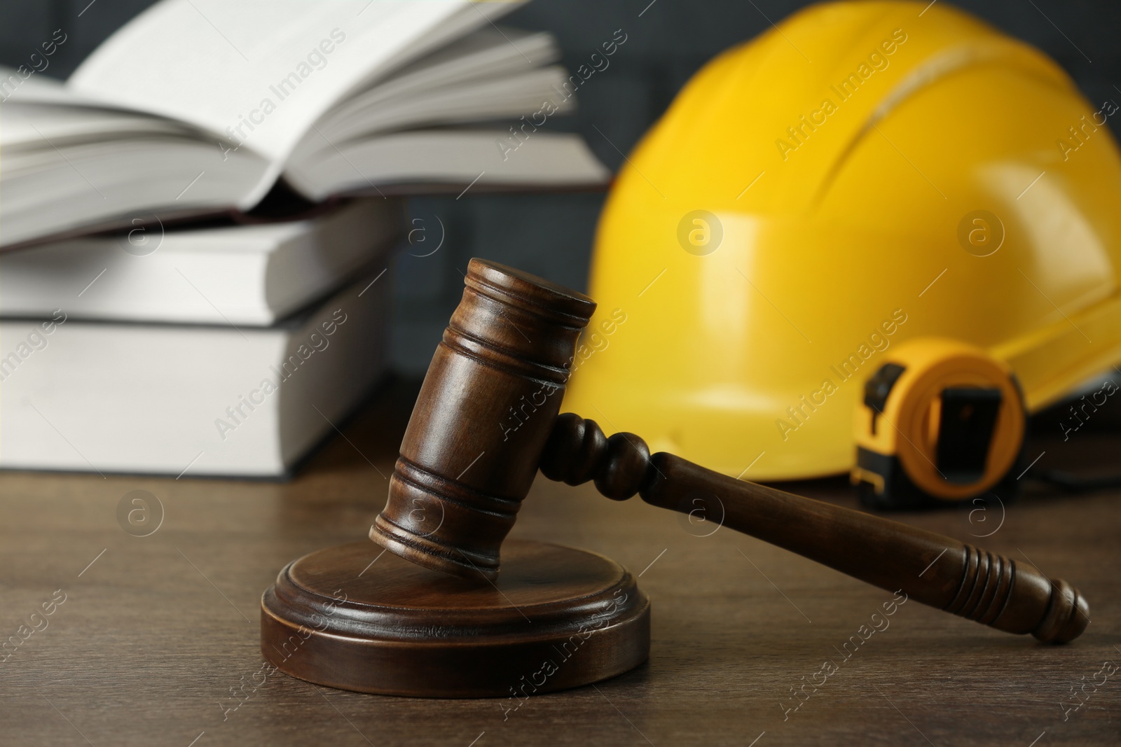 Photo of Construction and land law concepts. Gavel, hard hat, measuring tape and books on wooden table, closeup