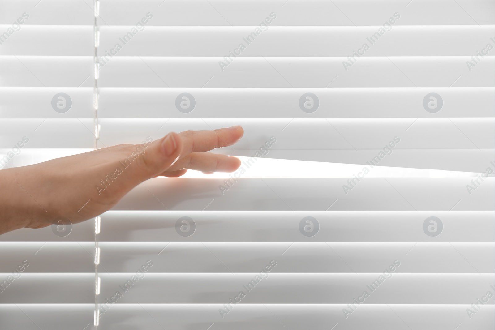 Photo of Young woman opening window blinds, closeup. Space for text