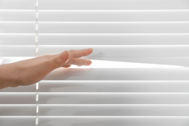 Photo of Young woman opening window blinds, closeup. Space for text