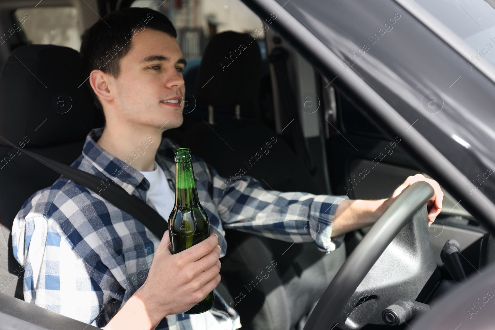 Photo of Smiling man with bottle of beer driving car, view from outside. Don't drink and drive concept