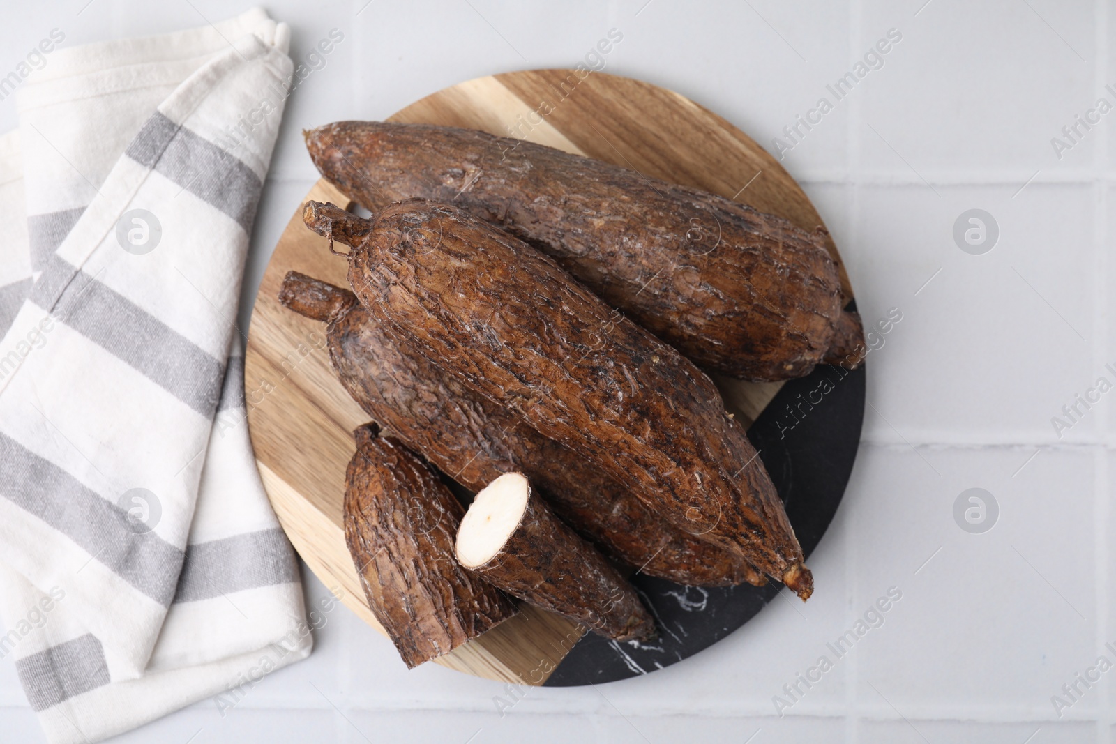 Photo of Whole and cut cassava roots on white tiled table, top view