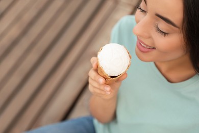 Happy young woman with delicious ice cream in waffle cone outdoors, closeup. Space for text