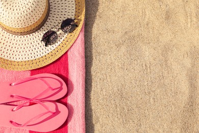 Beach towel with slippers, straw hat and sunglasses on sand, flat lay. Space for text