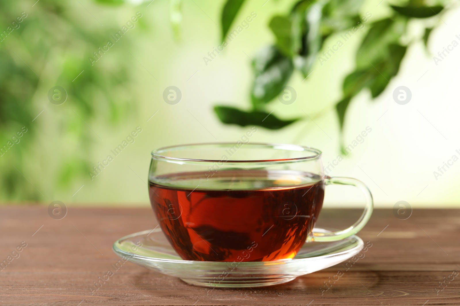 Photo of Cup of black tea on wooden table against blurred background. Space for text