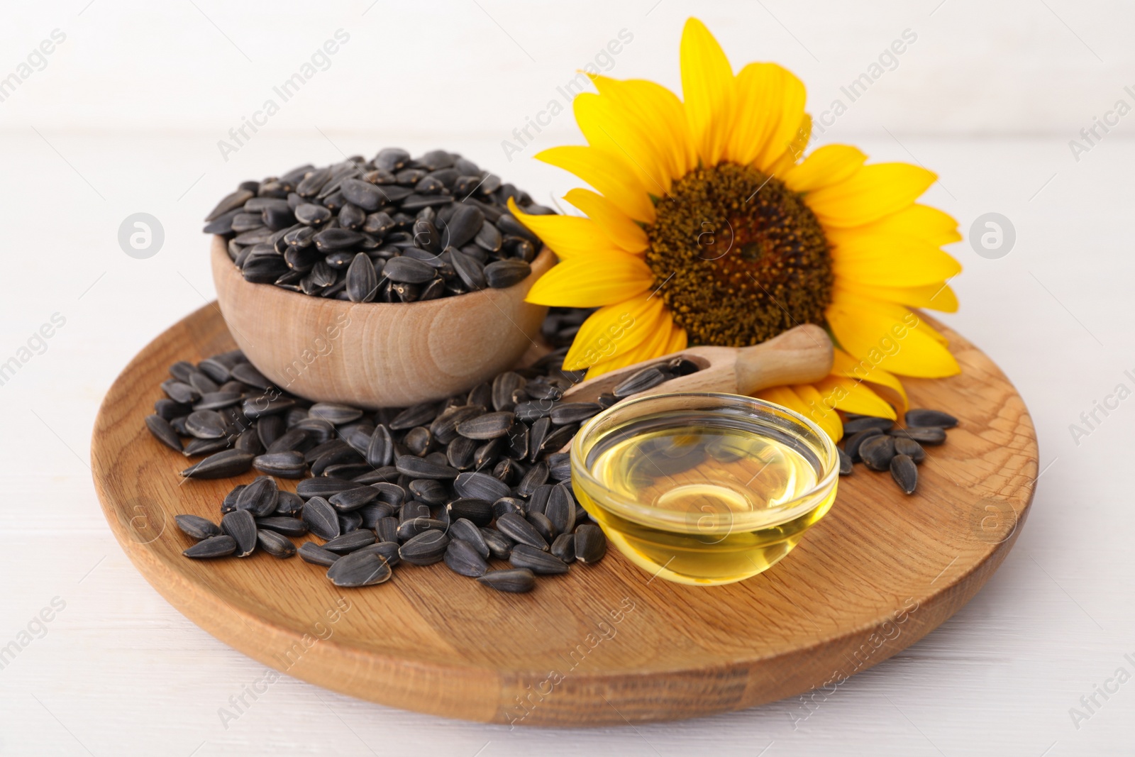 Photo of Sunflower, oil in glass bowl and seeds on white wooden table