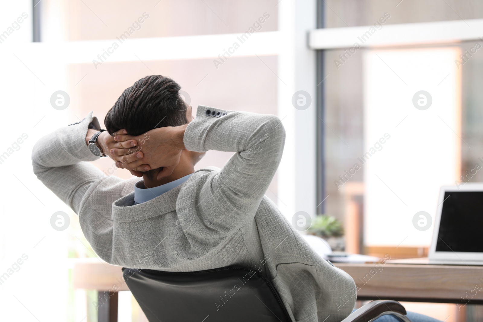 Photo of Businessman relaxing in office chair at workplace, back view. Space for text