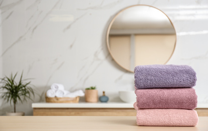 Stack of fresh towels on wooden table in bathroom. Space for text