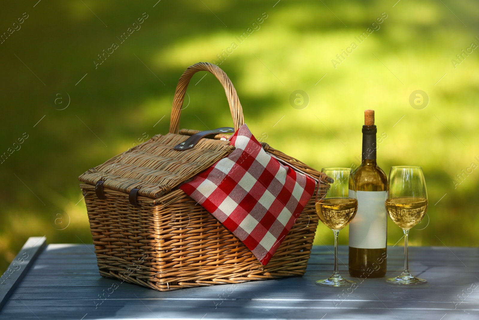 Photo of Wicker basket with blanket and wine on table in park. Summer picnic