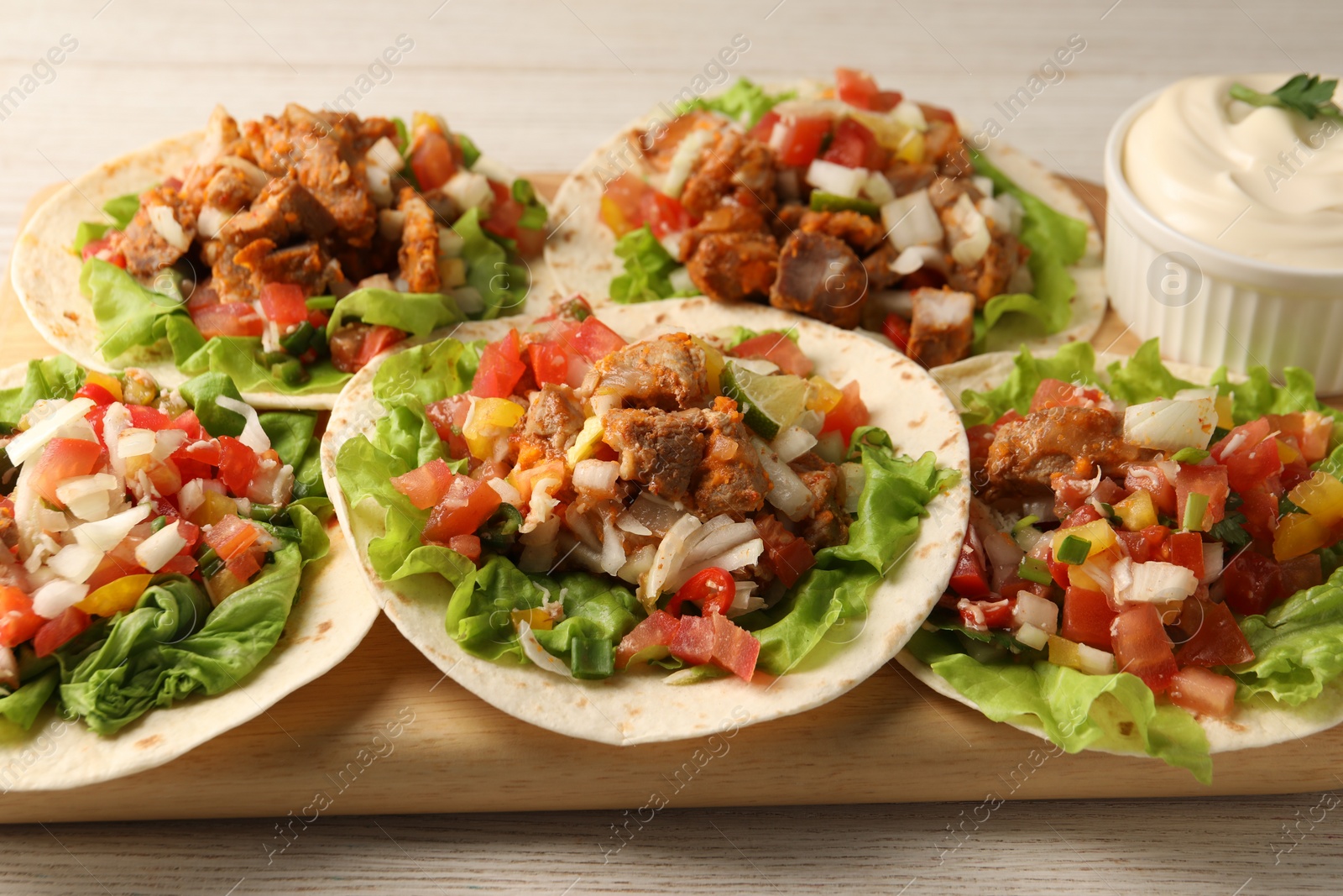 Photo of Delicious tacos with vegetables, meat and sauce on white wooden table