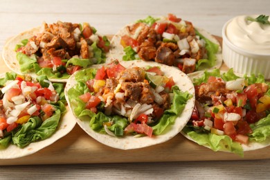 Photo of Delicious tacos with vegetables, meat and sauce on white wooden table