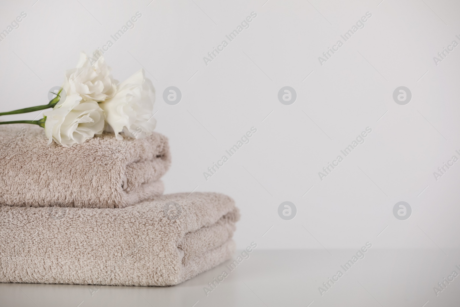 Photo of Soft folded towels and eustoma flowers on white table, space for text