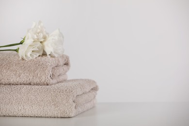 Soft folded towels and eustoma flowers on white table, space for text