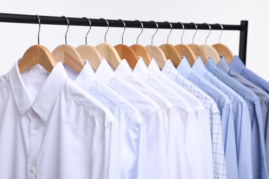 Photo of Dry-cleaning service. Many different clothes hanging on rack against white background, closeup