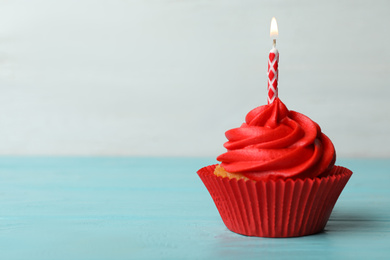 Delicious birthday cupcake with cream and burning candle on blue wooden table. Space for text