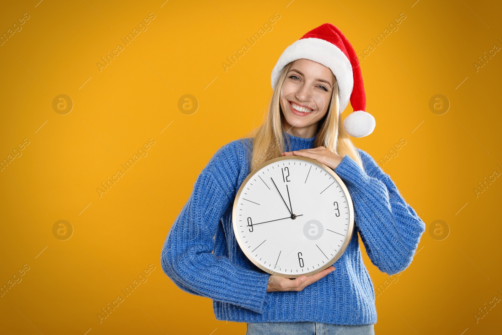 Photo of Woman in Santa hat with clock on yellow background, space for text. New Year countdown