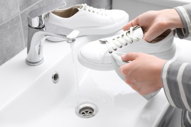 Photo of Woman washing stylish sneakers with brush in sink, closeup