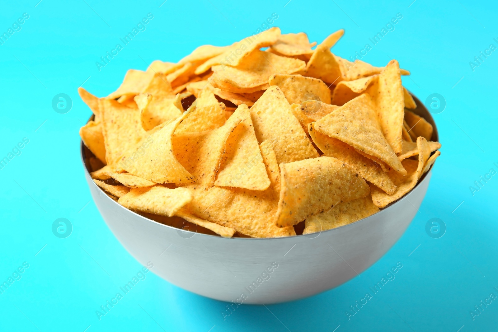 Photo of Tasty mexican nachos chips in metal bowl on blue background