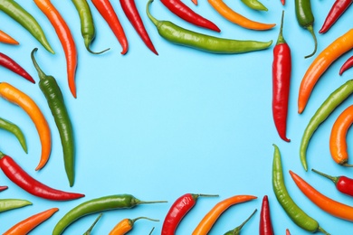 Frame made with different chili peppers on blue background, flat lay. Space for text