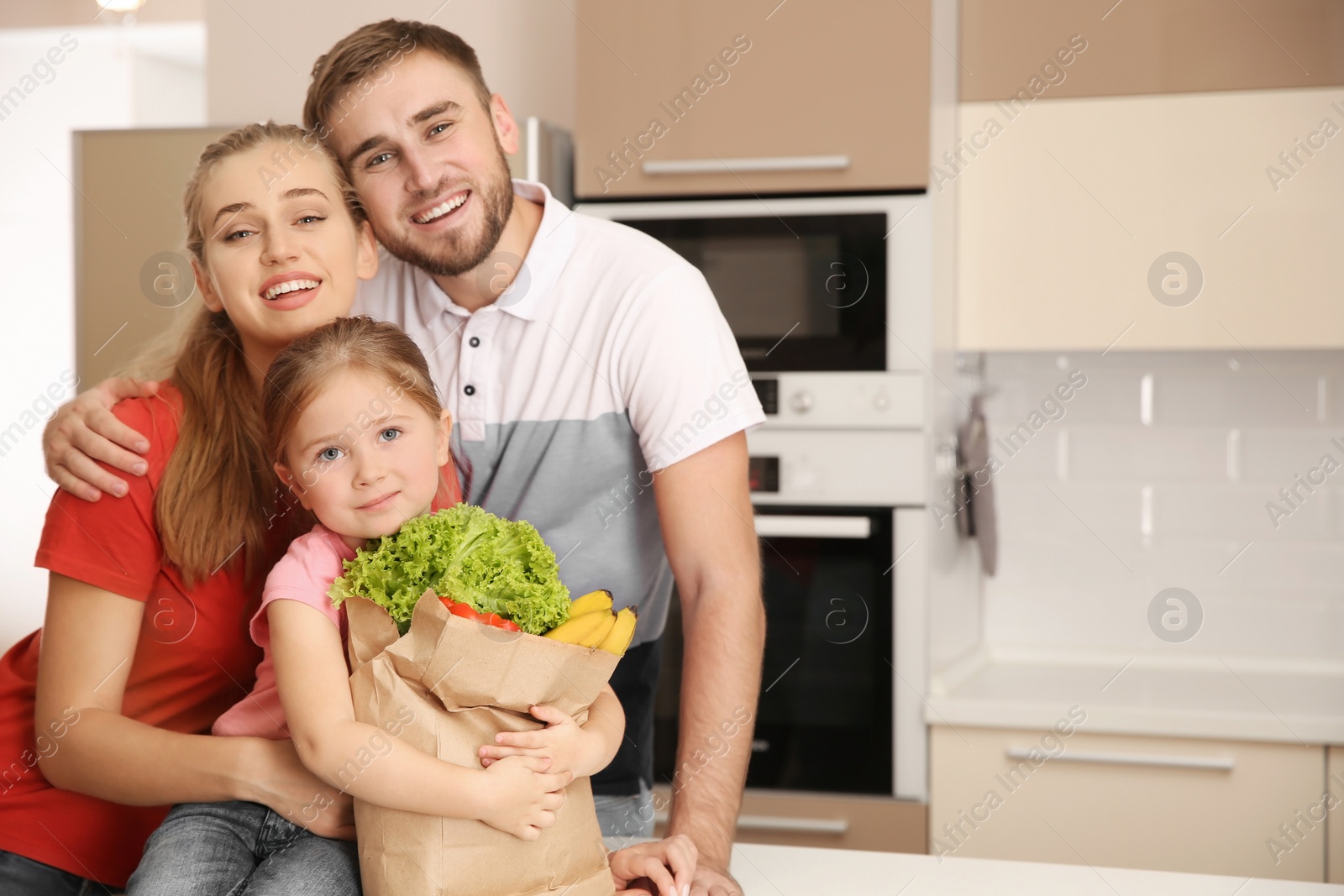 Photo of Happy young family with healthy food in paper bag at home