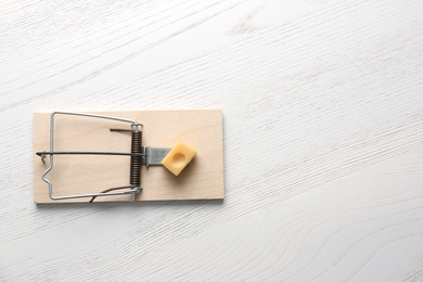 Photo of Mousetrap with piece of cheese and space for text on white wooden background, top view. Pest control