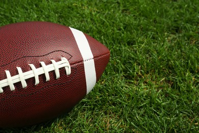 Photo of American football ball on green grass, closeup. Space for text