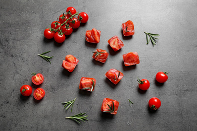 Photo of Ice cubes with tomatoes and rosemary on grey table, flat lay