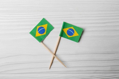 Photo of Small paper flags of Brazil on white wooden table, flat lay