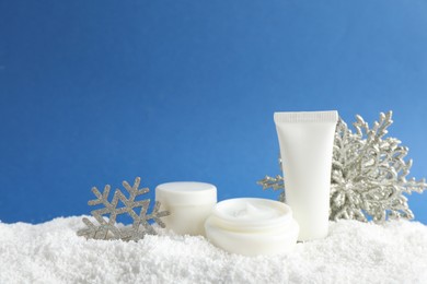 Photo of Set of winter skin care cosmetics with hand cream and decorative snowflakes on snow against blue background. Space for text