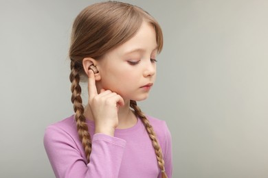 Little girl with hearing aid on grey background. Space for text
