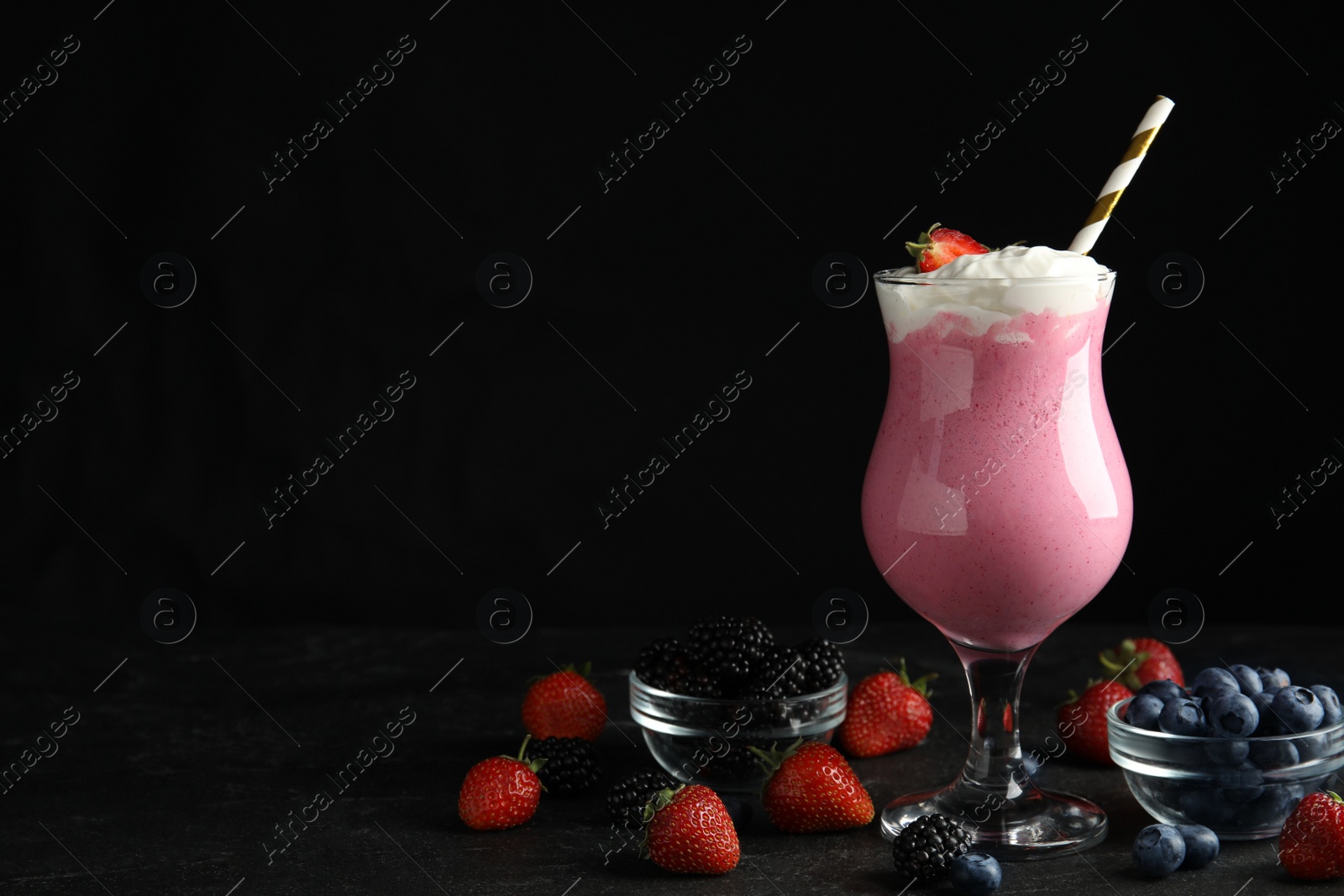 Photo of Tasty milk shake with whipped cream and fresh berries on black slate table. Space for text