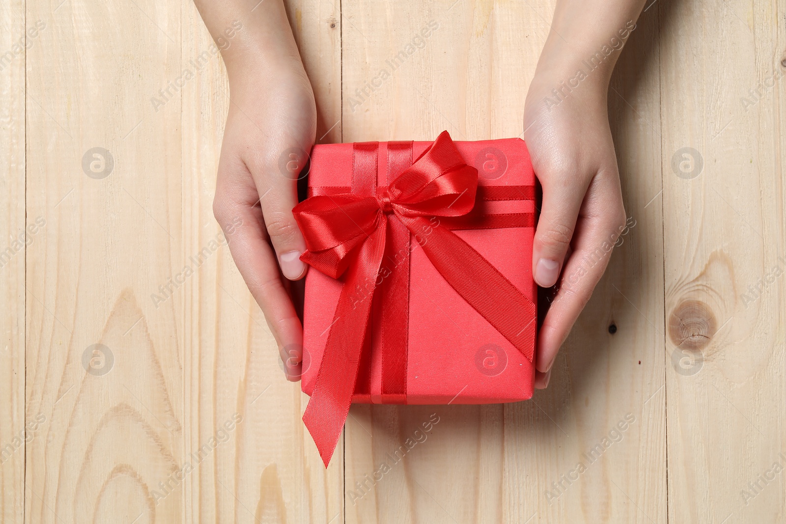 Photo of Christmas present. Woman holding gift box at wooden table, top view